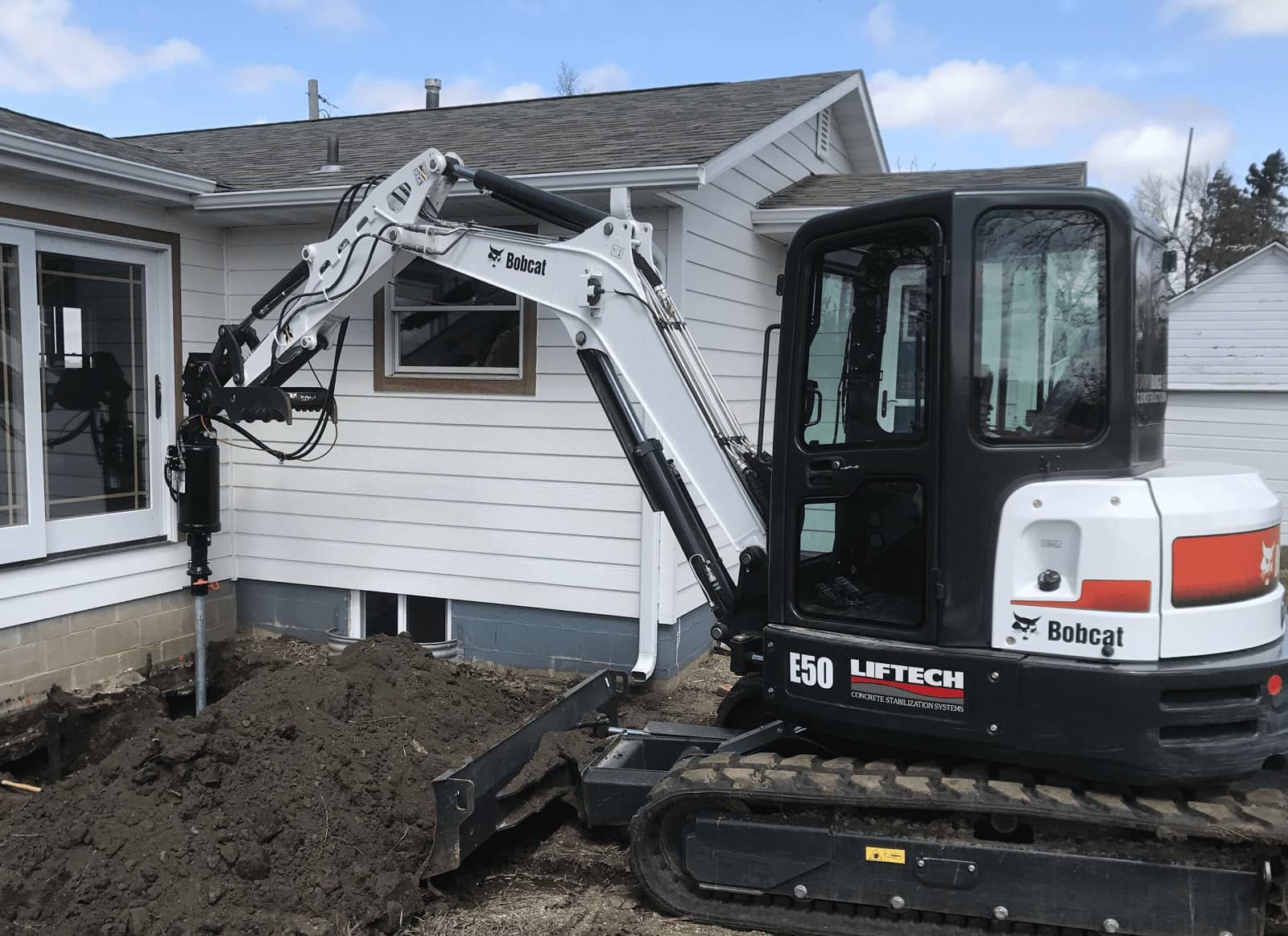 Liftech's Bobcat E50 mini excavator drilling a helical pier beside a house